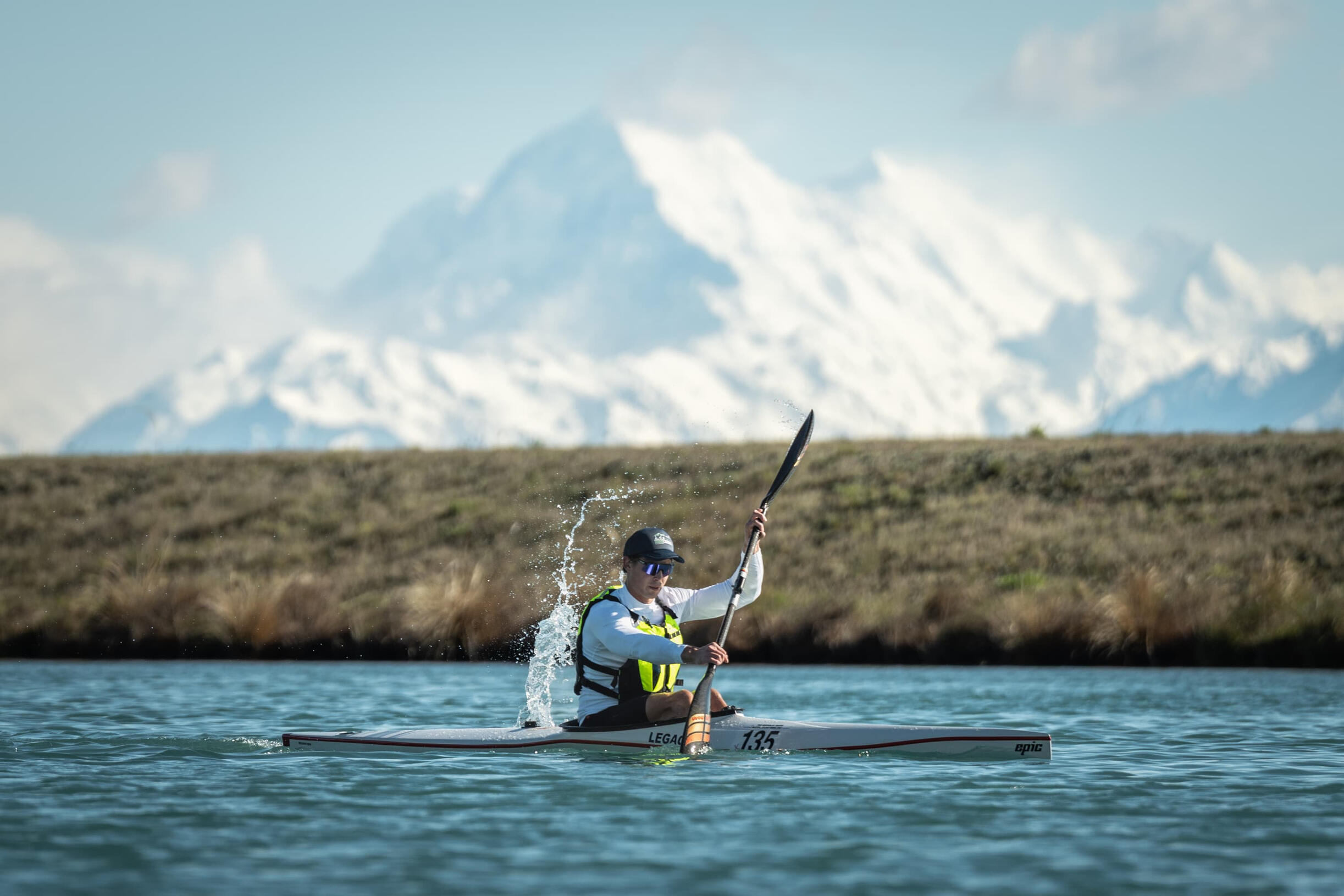 Meridian Twizel Hard Labour Triathlete in wetsuit and red swim cap exploding out of lake water at race start, mountains visible in background, dramatic splash and motion