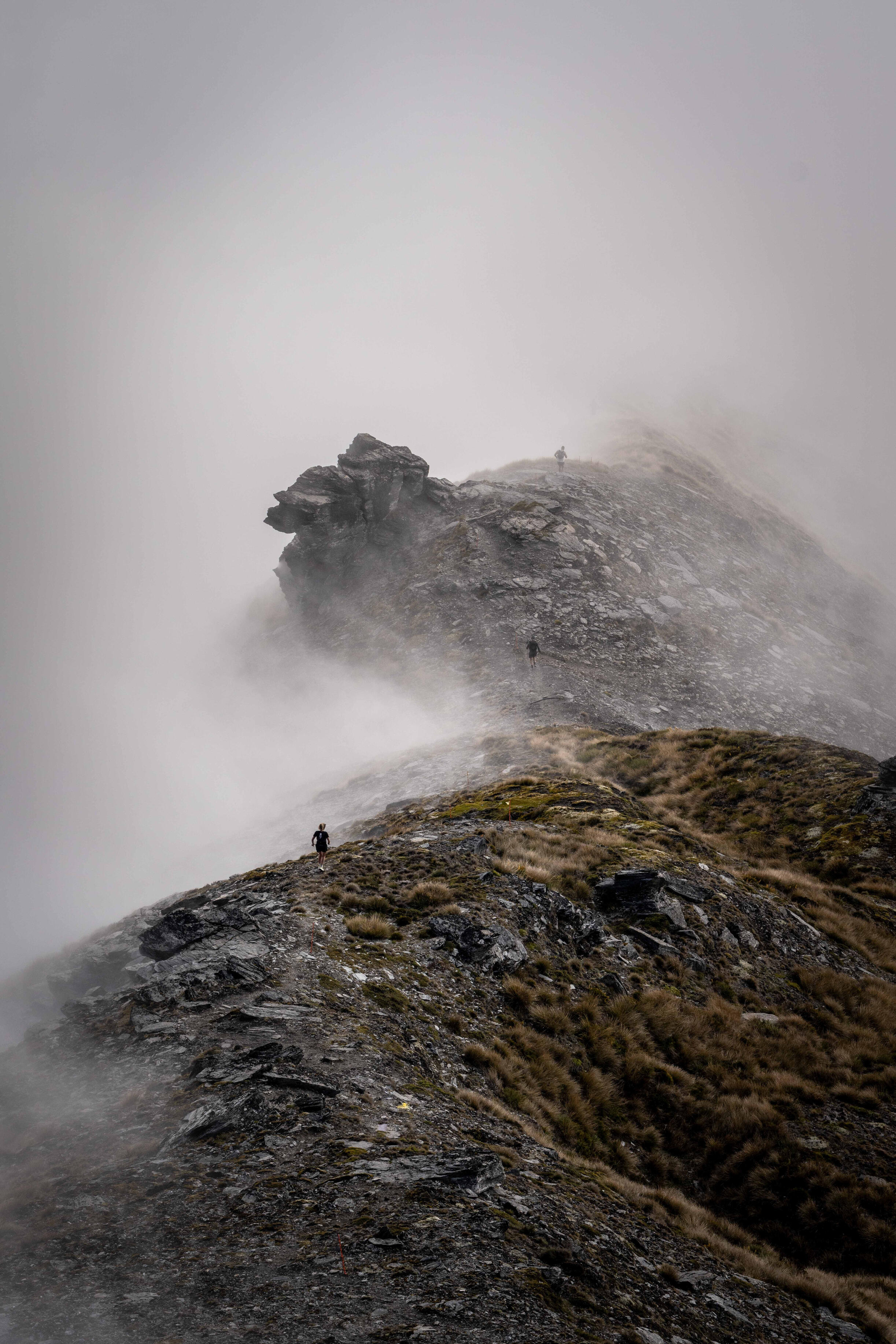 Runner Treble Cone Wanaka New Zealand Lone hiker standing on mountain ridge approaching rocky summit shrouded in swirling mist and fog, atmospheric alpine landscape